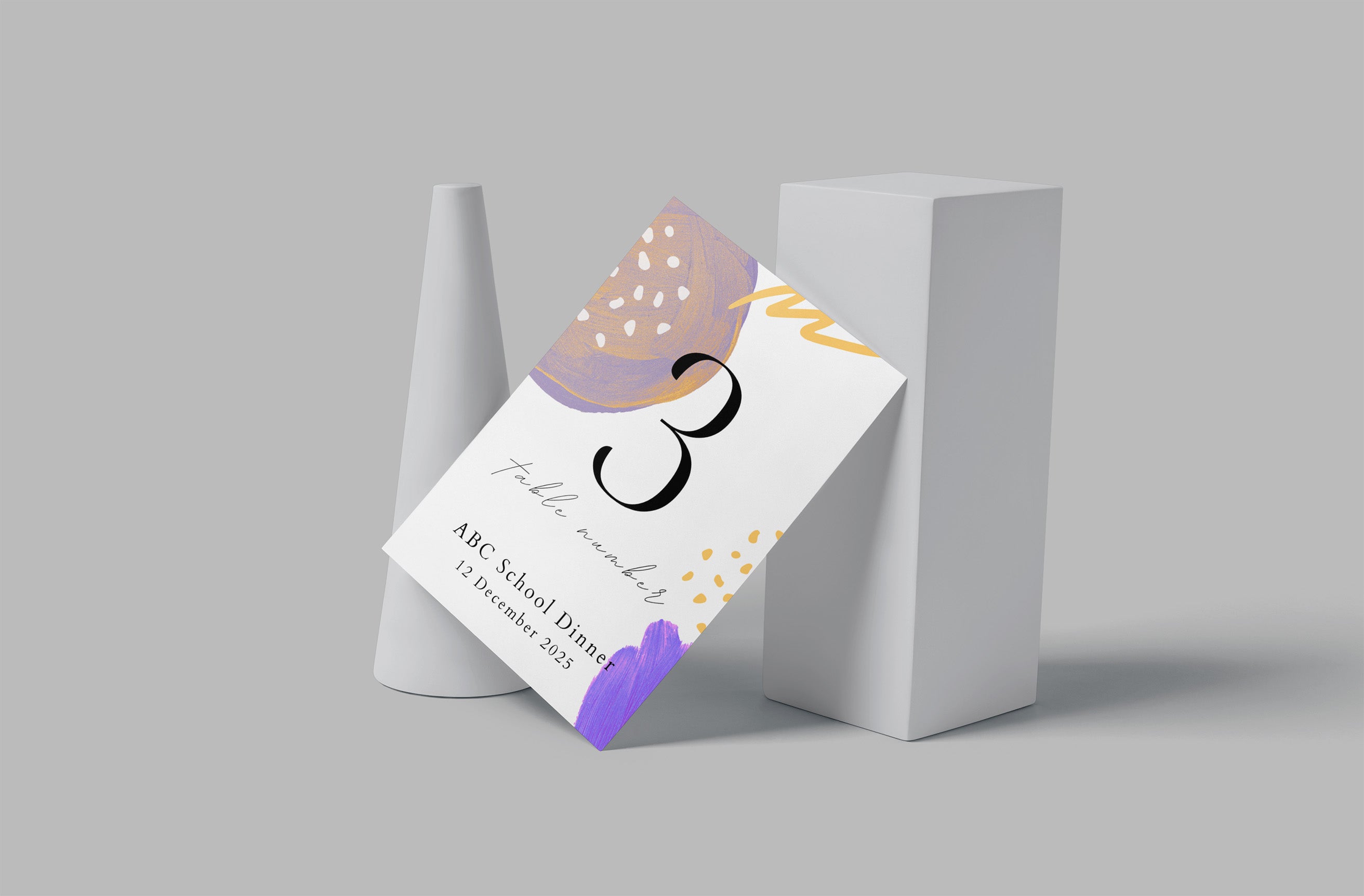 A printed invitation card or ticket with abstract pastel artwork and the number 3 leans against a white rectangular pedestal on a light gray background.