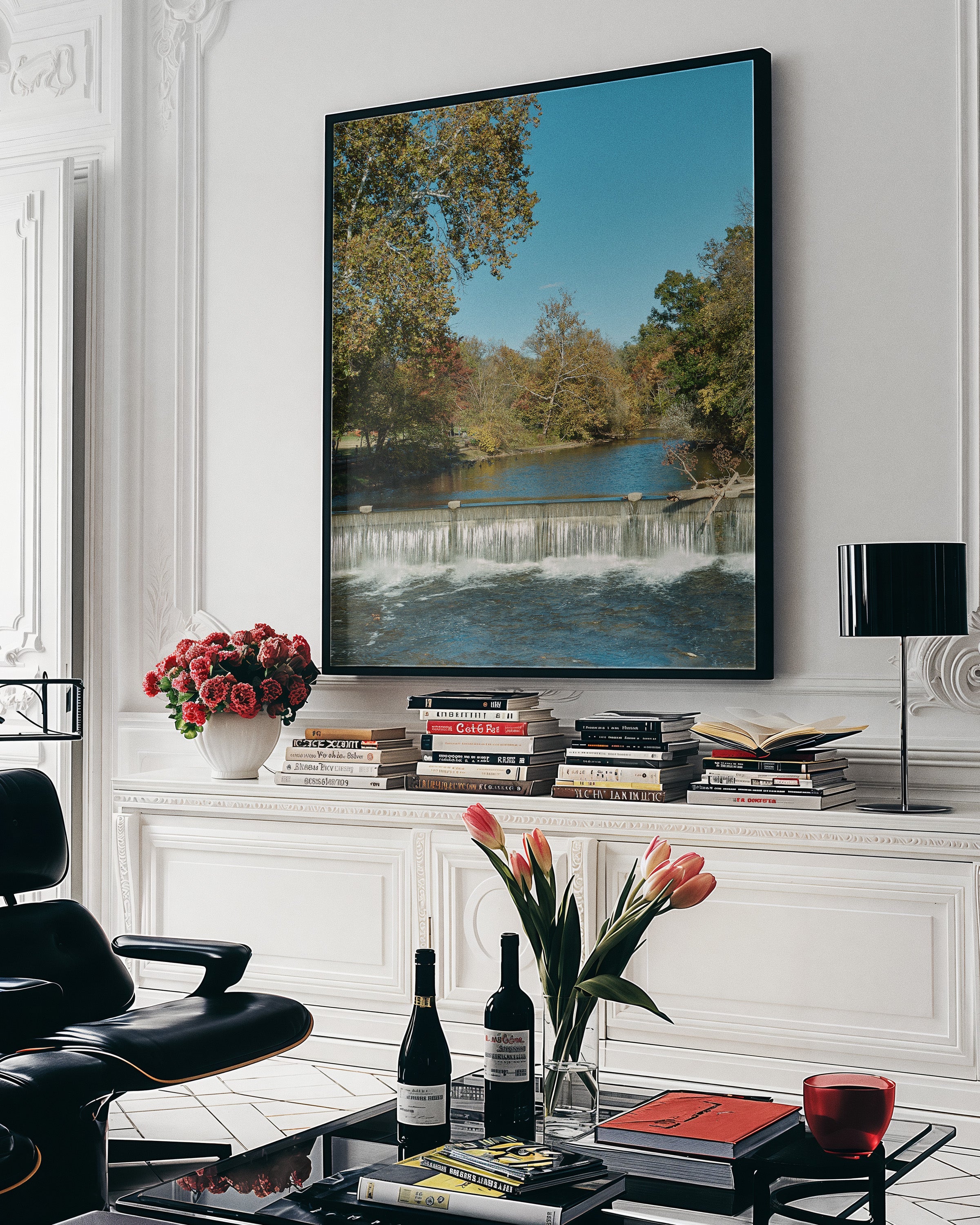 A large framed landscape art print depicting a waterfall and river surrounded by autumn trees, displayed on a white wall above a console table in a styled living room.