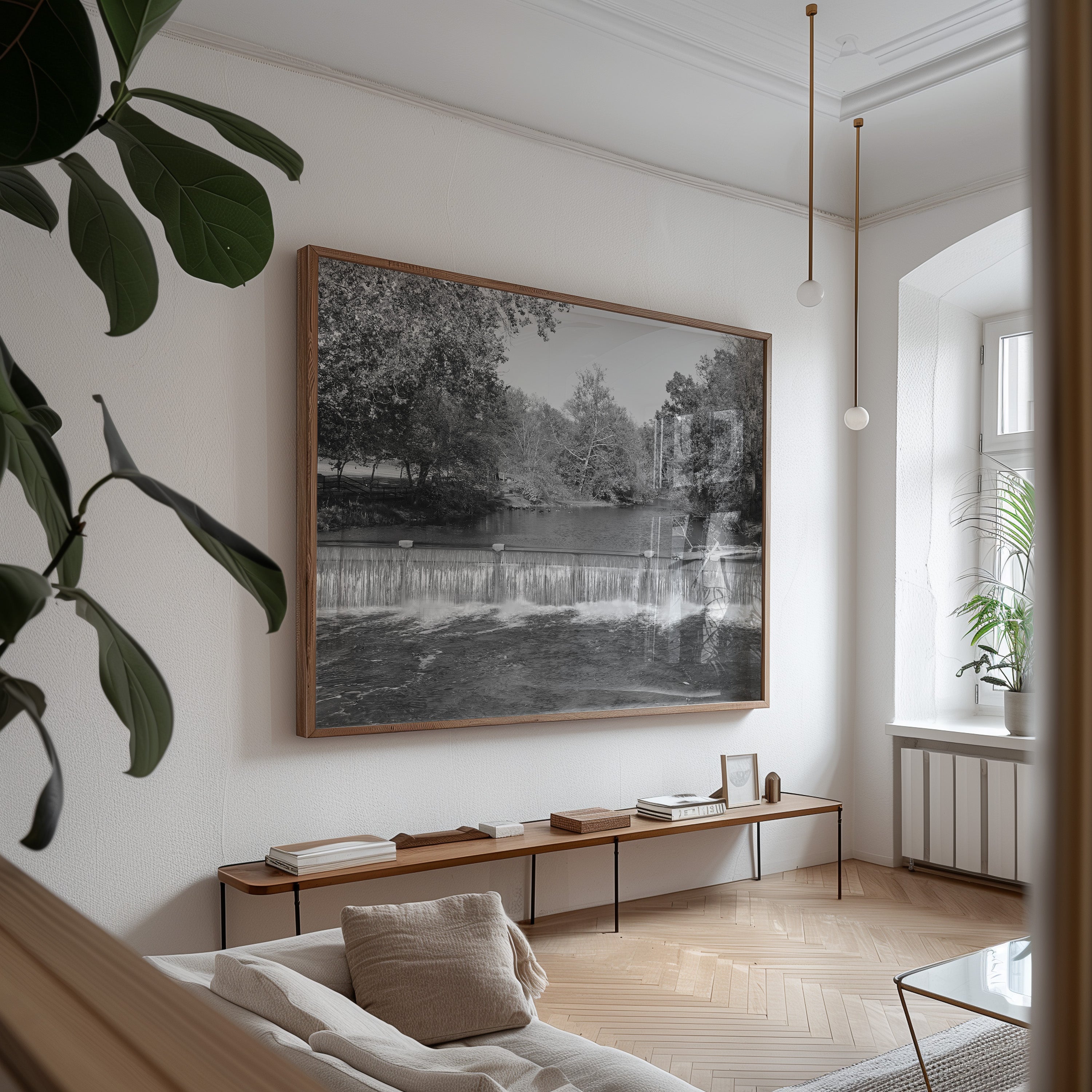 A large framed black and white landscape photograph of a waterfall and trees, displayed on a white wall in a modern, sunlit living room with a wooden bench and light wood flooring.