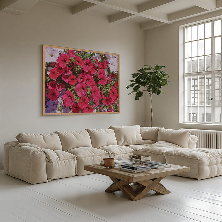 A large framed wall art print featuring a dense cluster of bright pink and red flowers hangs above a cream sectional sofa in a bright, modern living room with a wooden coffee table and a potted plant.