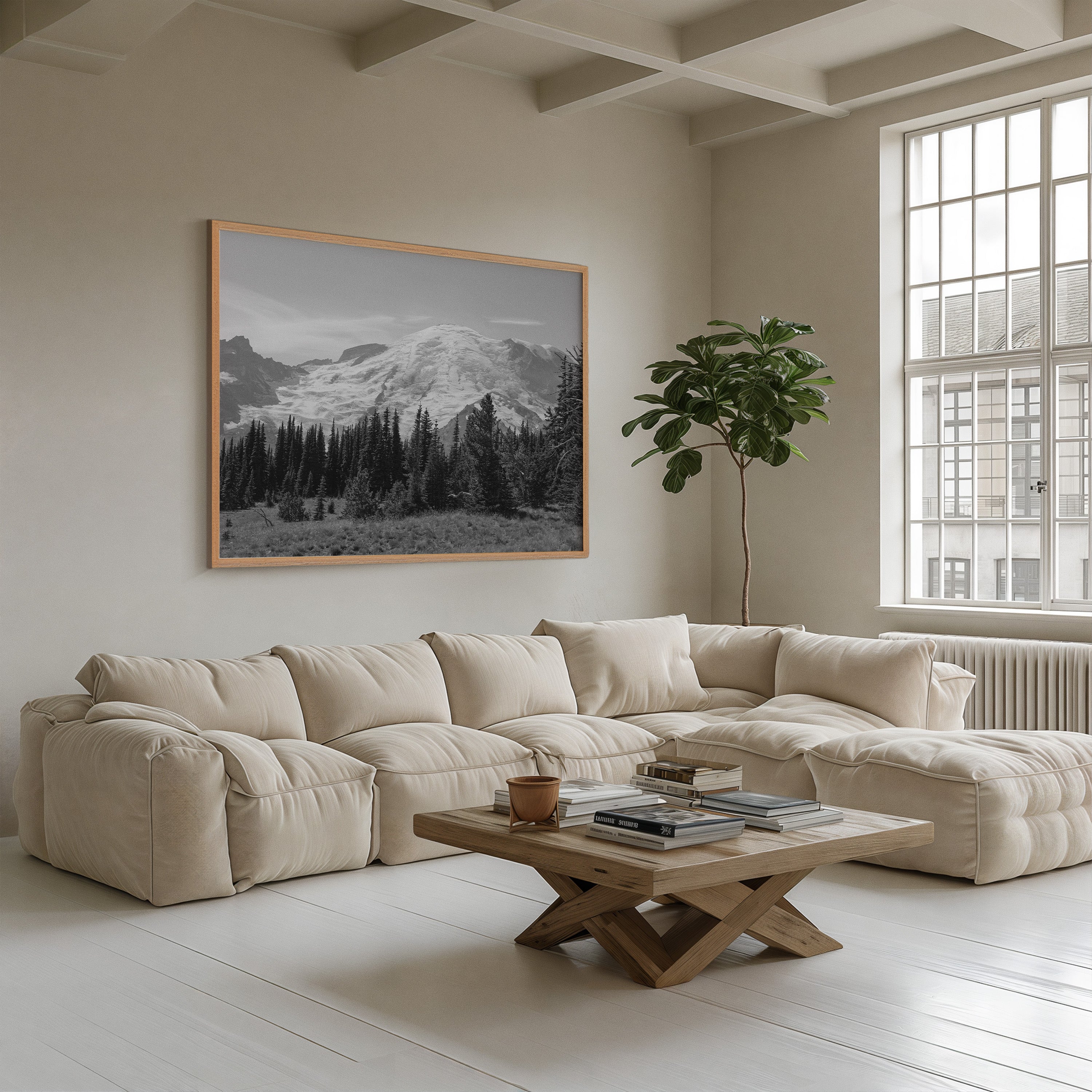 A large framed black and white landscape photograph of mountains and pine trees hangs on a beige wall above a cream tufted sectional sofa in a bright, modern living room.