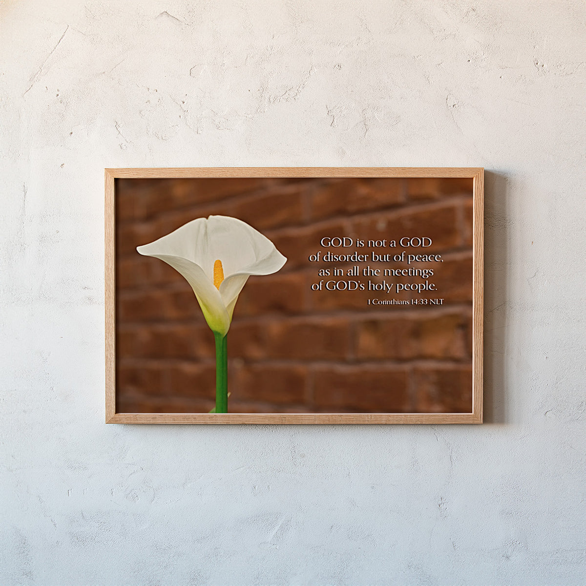 A framed wall art print featuring a white calla lily against a brown brick background, with a Bible verse printed on the right side. The frame is mounted on a textured off-white wall.