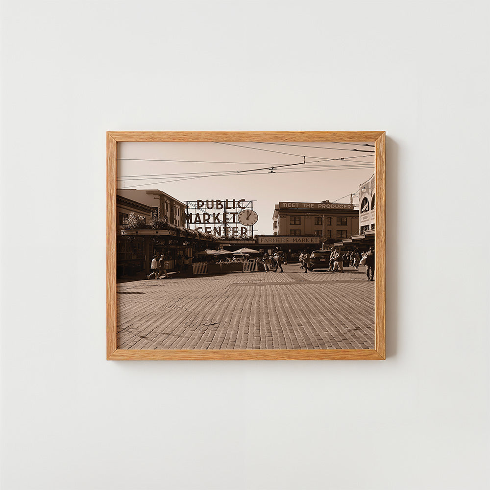 A framed sepia-toned art print depicting a vintage street market scene with a 'PUBLIC MARKET CENTER' sign, mounted on a light gray wall.