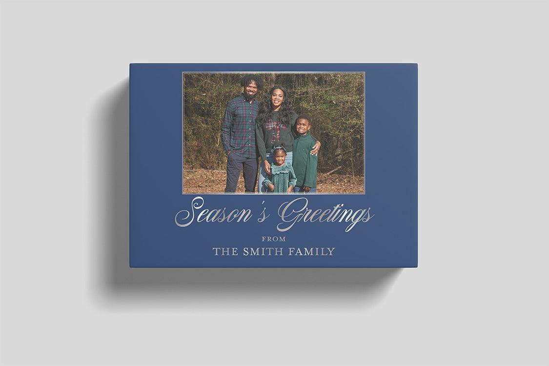 A blue holiday greeting card shown at an angle on a light gray background. The card features a central family photograph and the text 'Season's Greetings FROM THE SMITH FAMILY' in white script and serif fonts.