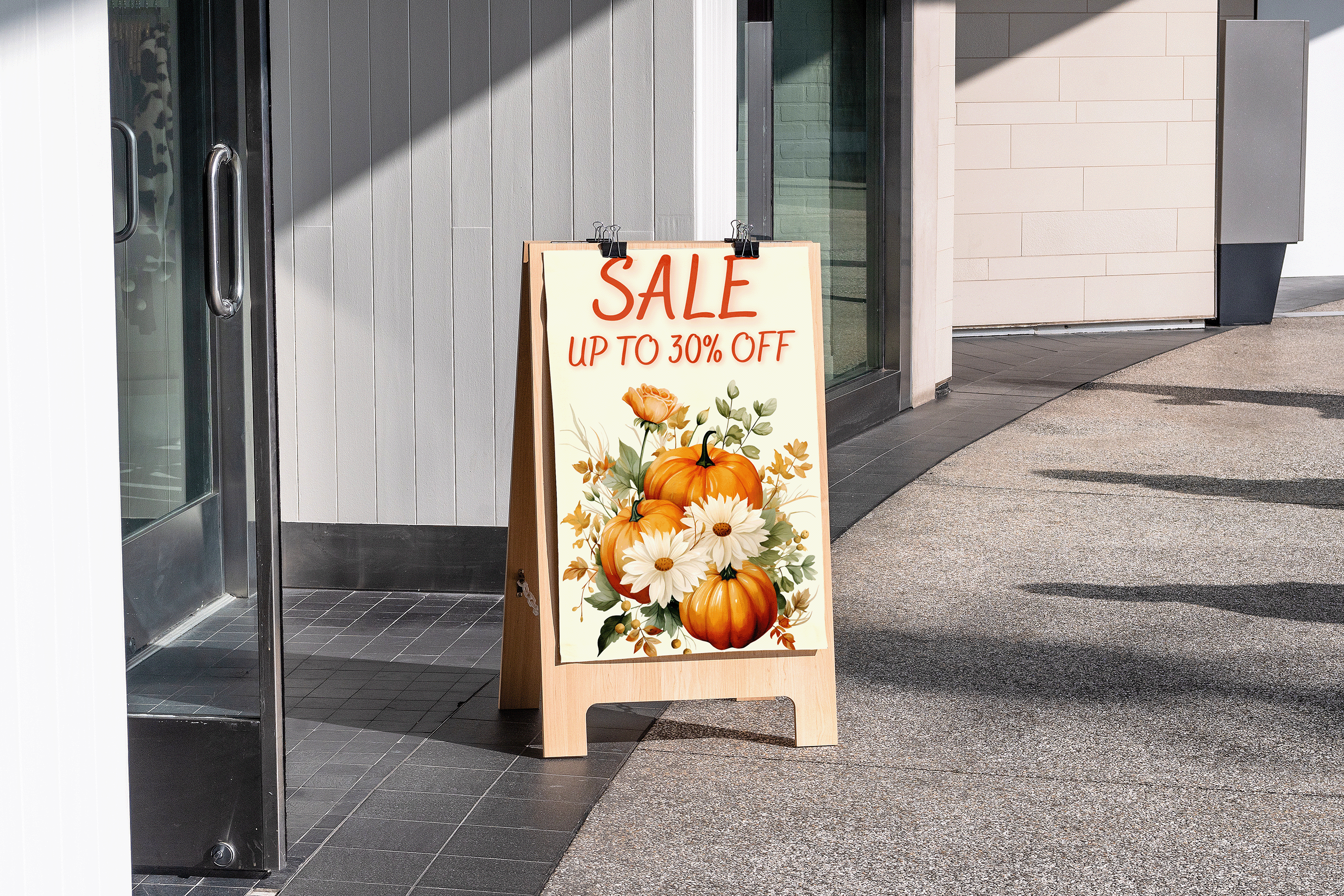 Outdoor sale sign with pumpkins and flowers in front of a building entrance.