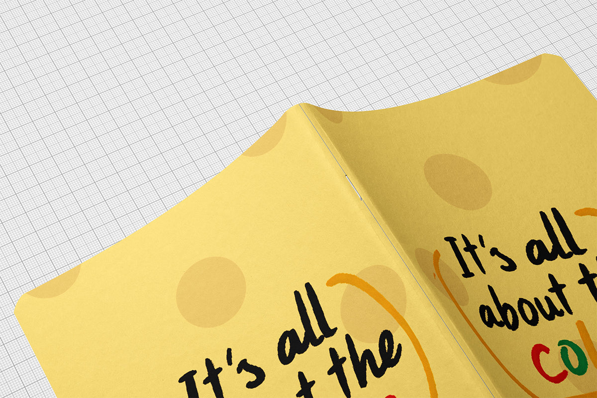 A close-up of a yellow squarefold journal with circular polka dots and handwritten text, shown on a white graph-paper background.
