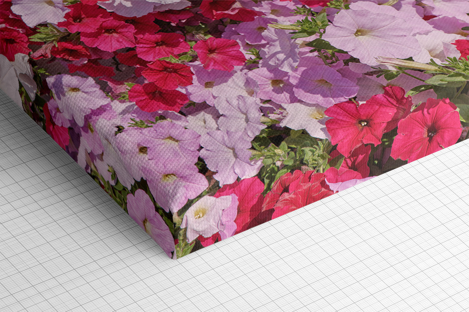 A rectangular box or package wrapped in a floral print featuring pink, red, and lavender petunias with green leaves, photographed on a white gridded surface.