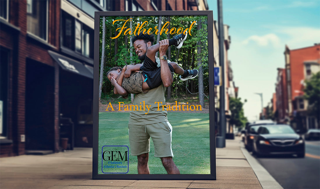 A framed custom photo print displayed on a city sidewalk. The print features a father carrying his child on his shoulders in a park, with the text 'Fatherhood A Family Tradition' and a 'GEM Custom Prints' logo at the bottom.