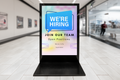 Digital display board in a shopping mall with 'We're Hiring' message.